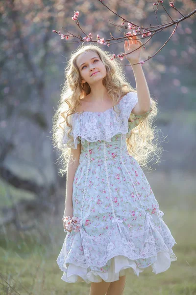 青いドレスを着ている花の咲く庭でポーズ美しい金髪少女 — ストック写真