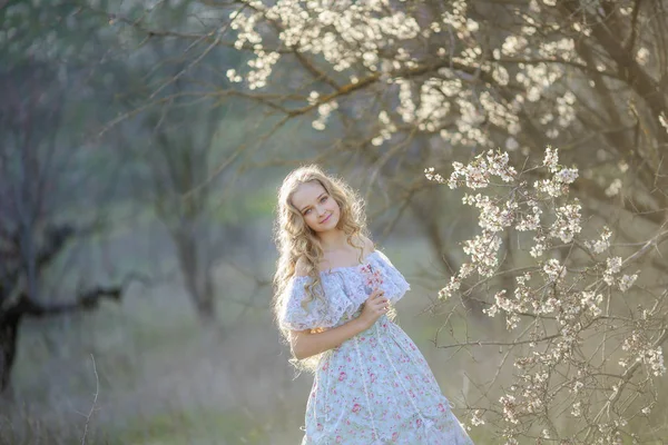 年轻美丽的金发女孩摆在盛开的花园穿着蓝色的礼服 — 图库照片