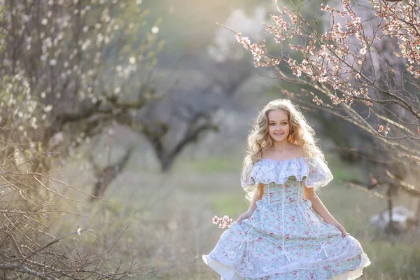 美丽的金发女孩穿着蓝色的礼服摆在盛开的花园 — 图库照片