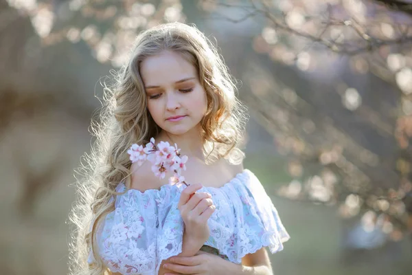 花の咲く庭でポーズ青いドレスを着ている美しいブロンドの女の子 — ストック写真