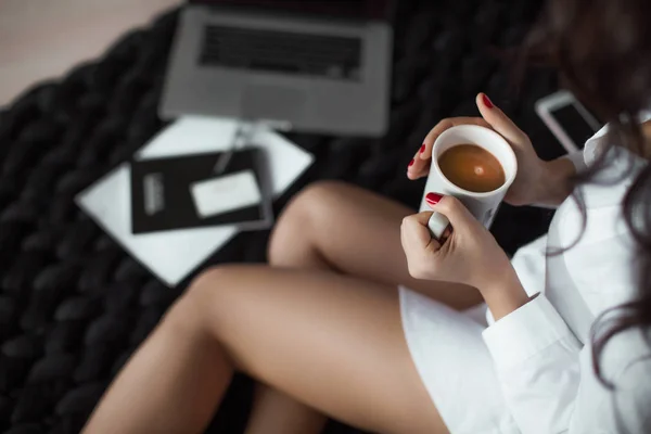 A cozy morning, a fluffy plaid, coffee, a laptop, and beautiful female feet