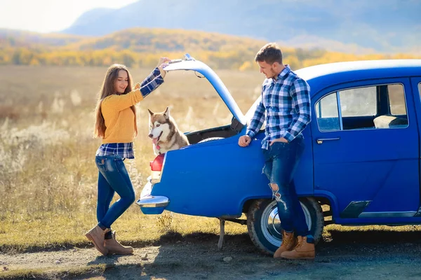 Erkek ve kadın mavi araba husky köpek ile poz 