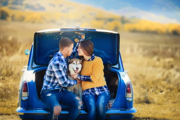 男性と女性が青い車でハスキー犬と一緒にポーズ — ストック写真