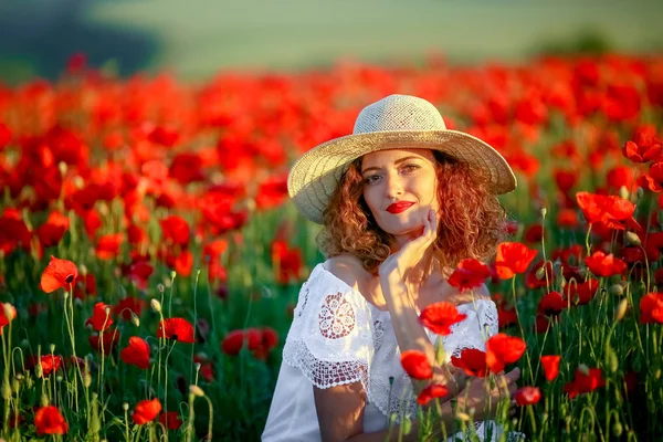若くてきれいな女性にケシ畑の身に着けている白いドレスと麦わら帽子でポーズ — ストック写真