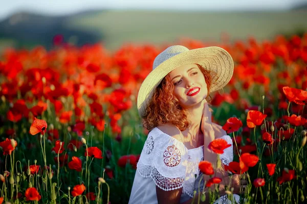 若くてきれいな女性にケシ畑の身に着けている白いドレスと麦わら帽子でポーズ — ストック写真