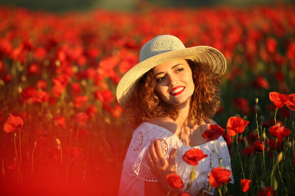 young beautiful woman posing on poppy field wearing white dress and straw hat 