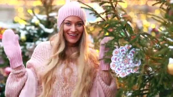 Una chica con un sombrero rosa y manoplas bailando cerca de un árbol de Navidad — Vídeos de Stock