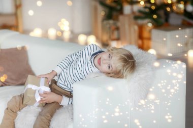 Noel ağacının arka planında sarı saçlı bir çocuk koltukta yatıyor ve en iyi Noel Baba hediyesinin hayalini kuruyor.