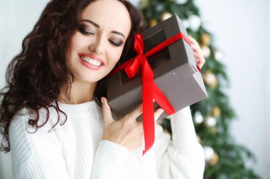 Kırmızı elbiseli bir kadın model bir fotoğraf stüdyosunda elinde bir yılbaşı hediyesi tutuyor.