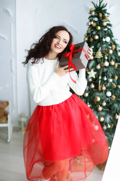 Női modell piros ruhában egy fotóstúdióban, kezében egy újévi ajándékkal. — Stock Fotó
