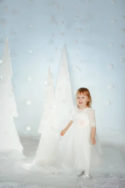 Cute girl in white Princess costume between white artificial glowing Christmas trees