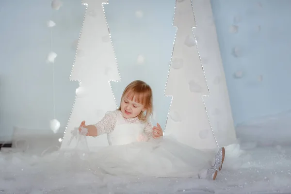 Schattig meisje in wit prinses kostuum tussen witte kunstmatige gloeiende kerstbomen — Stockfoto