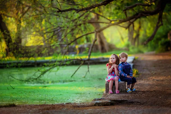 Niños un niño y una niña se sientan en el borde de un lago bosque artificial —  Fotos de Stock