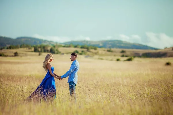 Um casal um homem e uma mulher em roupas bonitas em um campo dourado de trigo contra um fundo de pequenas montanhas — Fotografia de Stock