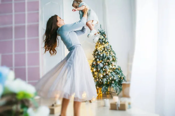 Familia de dos personas madre e hija 1 año de edad sobre el fondo de la foto del árbol de Navidad en colores brillantes — Foto de Stock