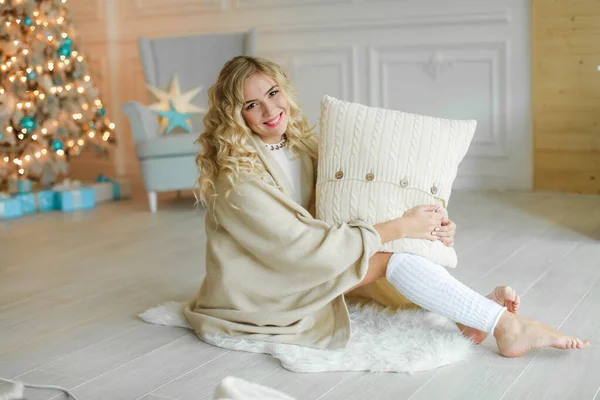 Een jonge blonde vrouw verpakt in een warme deken op de achtergrond van een kerstboom — Stockfoto