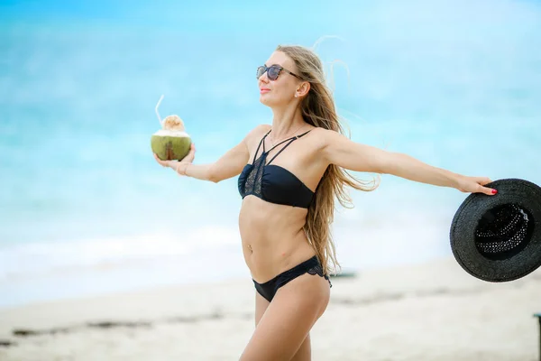 Plajda siyah mayolu bir kadın taze hindistan cevizi suyu içiyor. — Stok fotoğraf