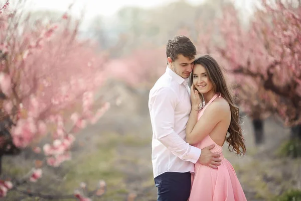 Romantischer Bräutigam küsst Braut auf die Stirn, während er an Wand steht, die mit rosa Blumen bedeckt ist — Stockfoto