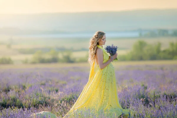 Hermosa mujer en un vestido largo amarillo y un ramo de lavanda en rui en un gran campo de lavanda — Foto de Stock