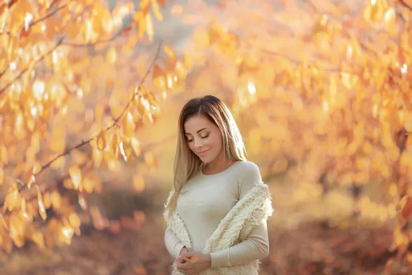 En kvinna i en vit varm tröja på bakgrunden av höstträd med gula blad — Stockfoto