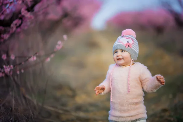 Roztomilá dívka v růžovém klobouku se zvonky v zahradě s broskví kvetoucí stromy — Stock fotografie