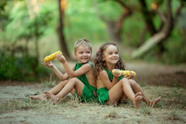 Çocuklar, erkek ve kız kardeşler yazın ormandaki bir açıklığa oturur ve mısır yerler.