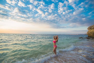 Young woman on the sea coast in a pink swimsuit in the background beautiful air clouds