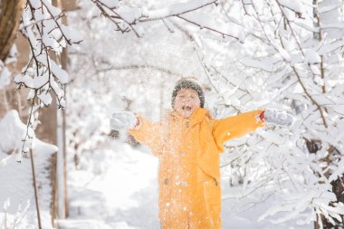 Açık havada, ormanda, parlak giysiler içinde bir çocuk Noel 'den bir gün önce karla oynuyor.