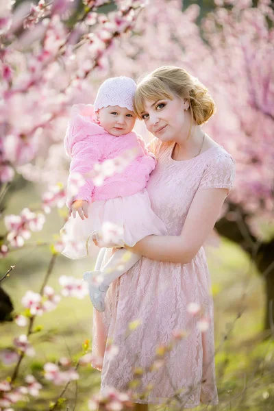 Мама и девушка в розовых платьях гуляют и веселятся в природном саду весной — стоковое фото