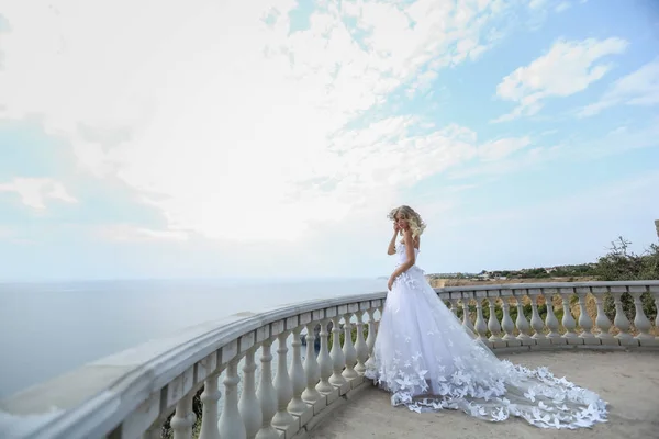 Een bruid in een prachtige witte trouwjurk staat op een balkon op de top van een berg op een zonnige zomerdag — Stockfoto