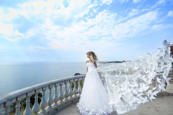 Een bruid in een prachtige witte trouwjurk staat op een balkon op de top van een berg op een zonnige zomerdag — Stockfoto