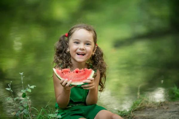 Dziewczyna z włosami plecione jedzenie arbuza w pobliżu jeziora — Zdjęcie stockowe