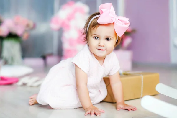 Bebê com um vestido rosa em um fundo de adorno rosa com um laço rosa na cabeça — Fotografia de Stock
