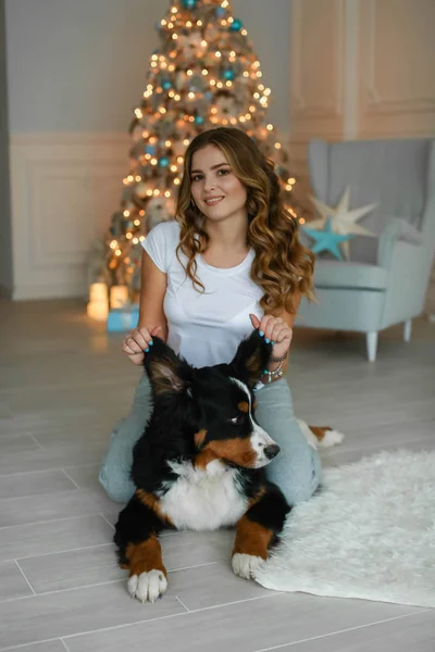 Kvinna med en stor hund i de nya åren kväll på bakgrunden av rummet med en julgran — Stockfoto