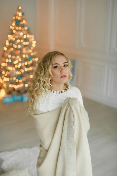 En ung blond kvinna insvept i en varm filt på bakgrunden av en julgran — Stockfoto