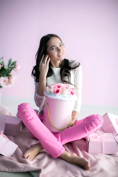 Um modelo feminino bonito novo senta-se em um tapete rosa com um buquê de flores em um pote de papelão — Fotografia de Stock