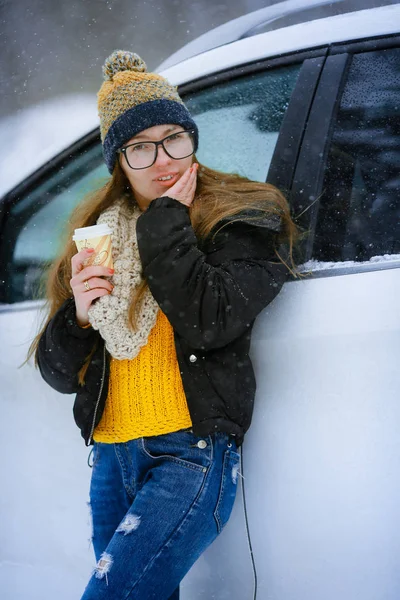 Una mujer en un coche blanco vestida con ropa de abrigo bebiendo café —  Fotos de Stock