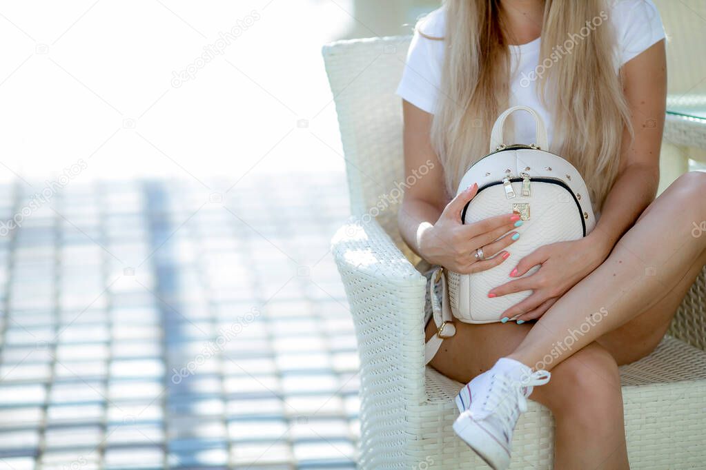 Blonde woman with long hair in beautiful legs sitting outdoors in a chair on vacation