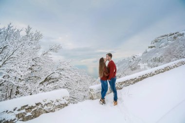 Bir adam kışın sıcak giysiler içinde durur ve soğuk havalarda onu ısıtan bir kadına sarılır.