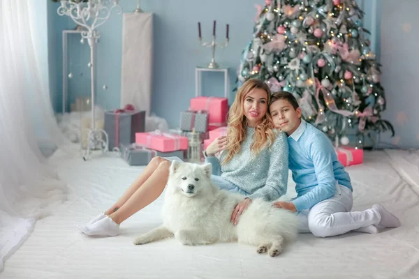 Vacker mor i en blek blå klänning och son 13 år gammal på bakgrunden av en julgran i ett blått rum — Stockfoto