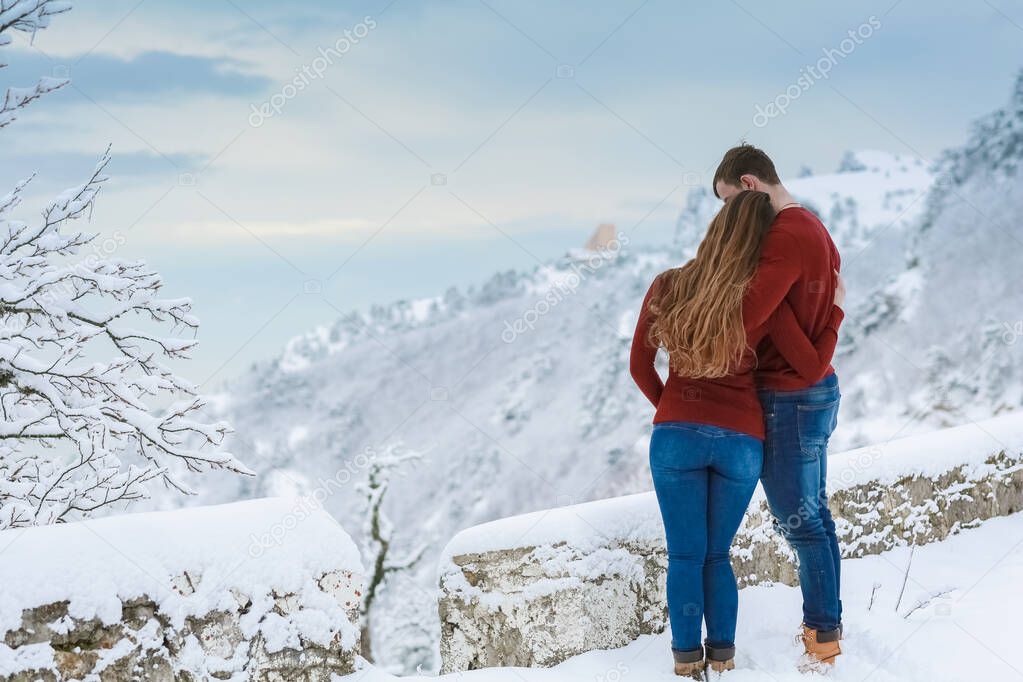 A man stands in warm clothes in winter and embraces a woman warming her with his warmth in cold weather