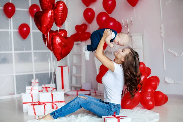 Une jeune famille de deux ou trois personnes célébrant un anniversaire de bébé fils dans une chambre blanche avec des ballons rouges — Photo