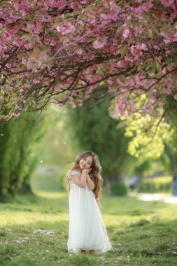 Beyaz kreşli bir çocuk yeşil çimlerin üzerinde beyaz bir elbise giyiyor.