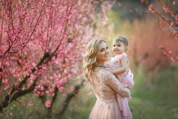 Beautiful young mom with white hair in the garden with pink trees her baby in her arms — Stock Photo, Image