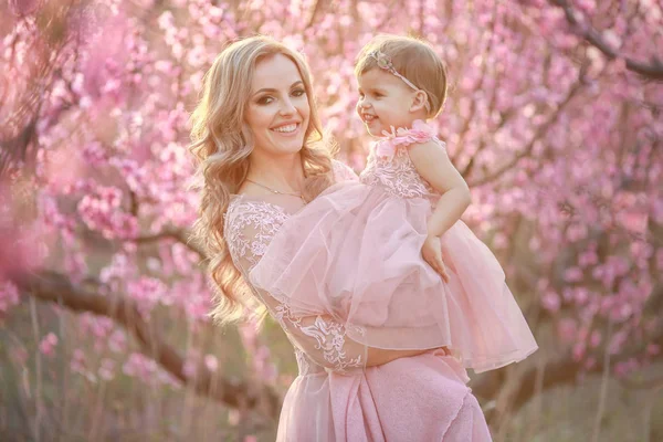 Egy nő rózsaszín menyasszonyi ruhában a kertben egy babával a karjában. — Stock Fotó