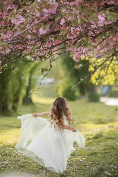 Een kind in een witte kleuterschool jurk op het groene gras in een openbaar park draagt een witte jurk — Stockfoto