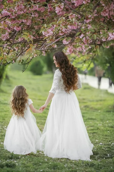 Мати одягнена в білу сукню, як наречена гуляє в парку зі своєю дочкою — стокове фото