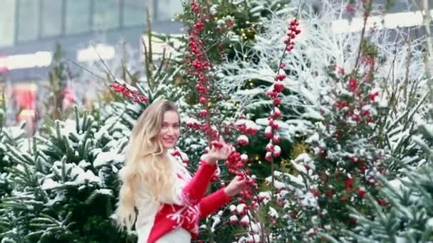 Chica en la calle en el fondo de los árboles de Navidad y bayas rojas — Vídeos de Stock