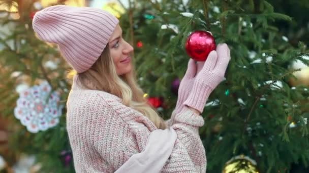 Ein Mädchen im rosafarbenen Pullover hält ein Weihnachtsbaumspielzeug auf der Straße — Stockvideo