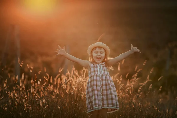 Chica rubia joven jugando con la luz del sol en los campos puesta de sol con un vestido con colina en el fondo — Foto de Stock